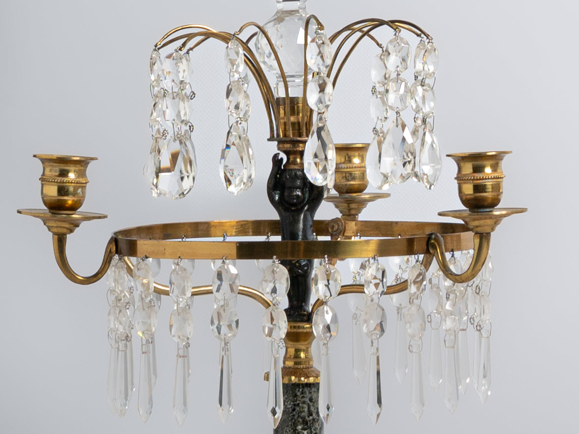 Par de girandoles de 3 lumes em metal dourado, vidro e cristal. Fustes decorados com “putto” e base em mármore. Séc. XIX