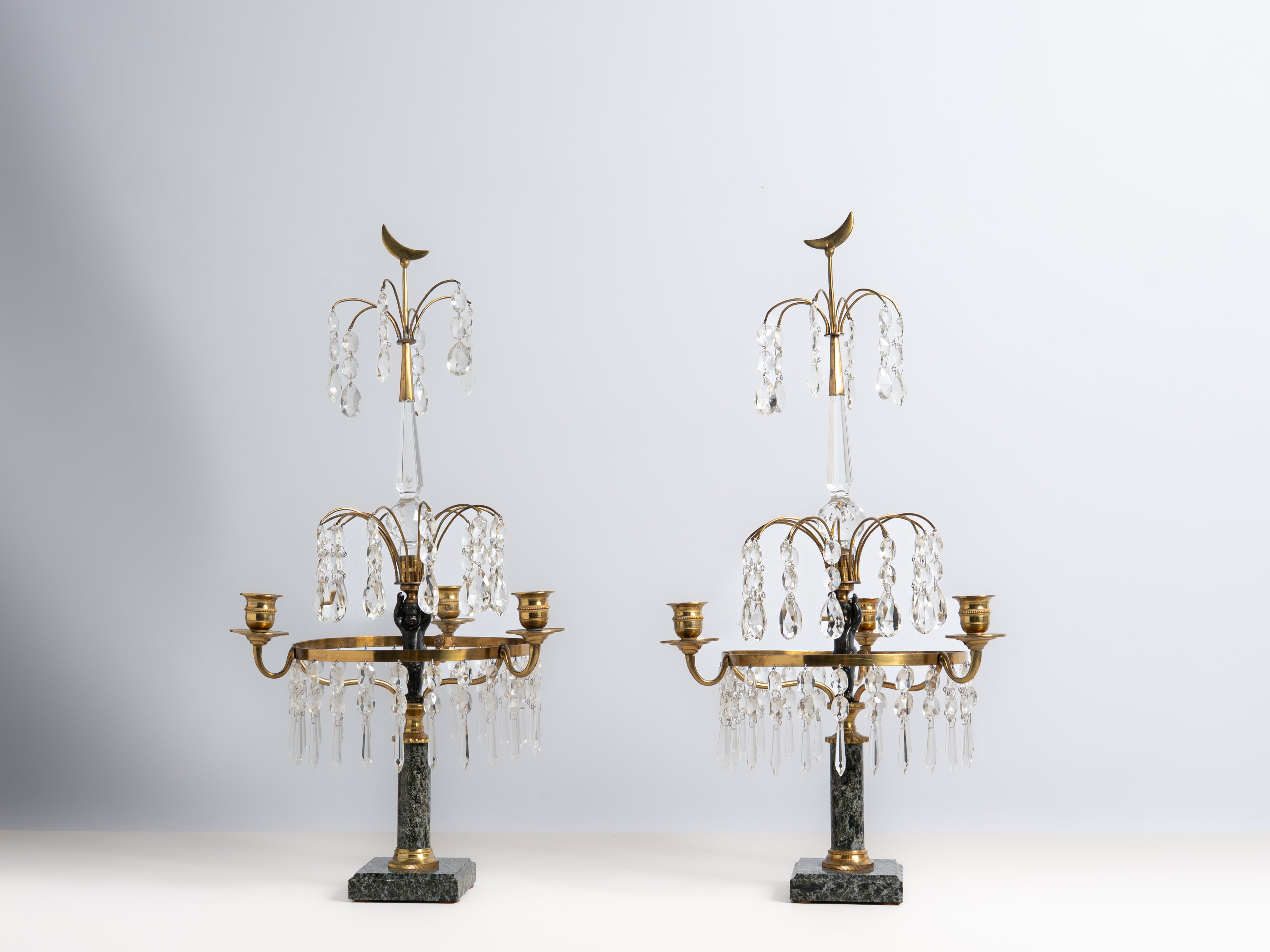 Par de girandoles de 3 lumes em metal dourado, vidro e cristal. Fustes decorados com “putto” e base em mármore. Séc. XIX